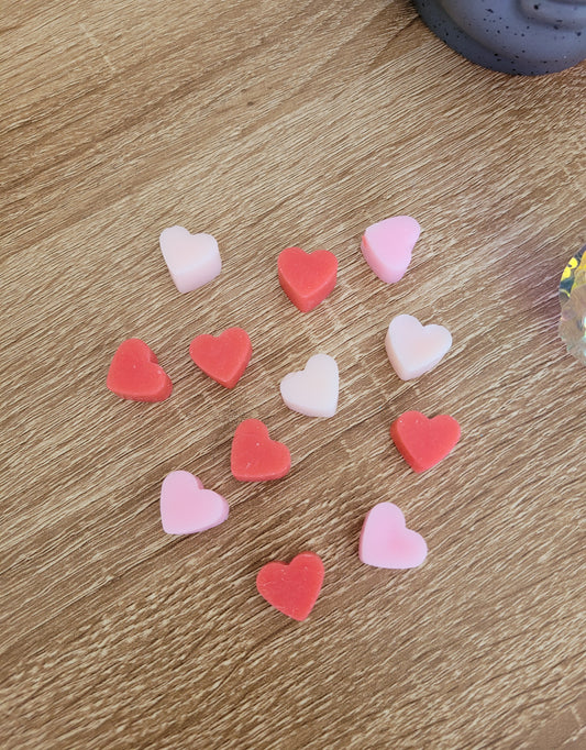 Gros plan sur des petits fondants en forme de cœurs, de couleurs rose, rouge et blanc, délicatement disposés, évoquant la douceur et la fraîcheur du parfum Coquelicot Sauvage.