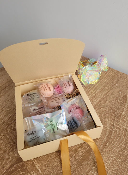 Assortiment de 10 fondants parfumés faits main aux couleurs variées, présentés dans un coffret ouvert sur fond décoratif.