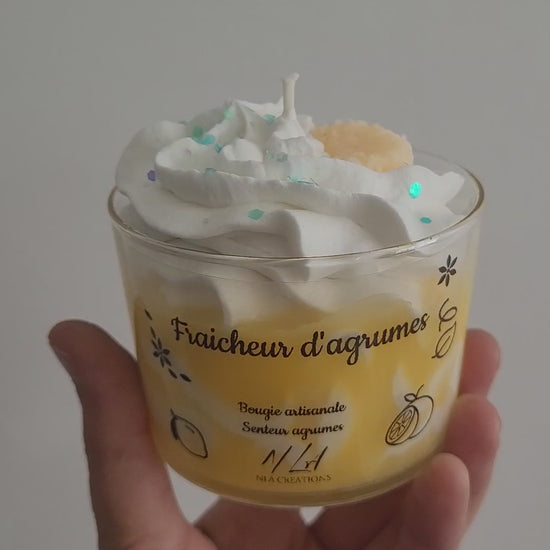  Vidéo d’une bougie couleur miel avec chantilly blanche et paillettes bleues, tournée lentement dans une main pour montrer ses détails et sa texture scintillante. 


