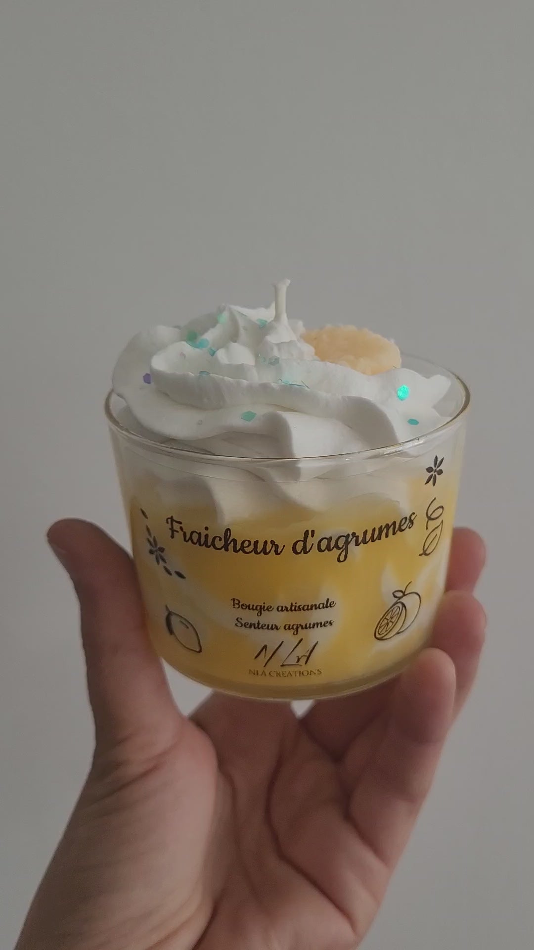  Vidéo d’une bougie couleur miel avec chantilly blanche et paillettes bleues, tournée lentement dans une main pour montrer ses détails et sa texture scintillante. 

