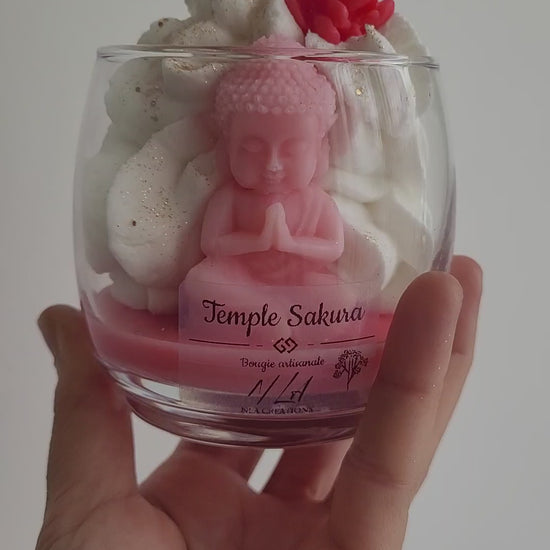 Bougie rose à la fleur de cerisier, avec figurine de Bouddha visible dans la cire et ambiance zen apaisante.