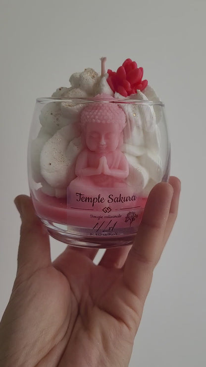 Bougie rose à la fleur de cerisier, avec figurine de Bouddha visible dans la cire et ambiance zen apaisante.