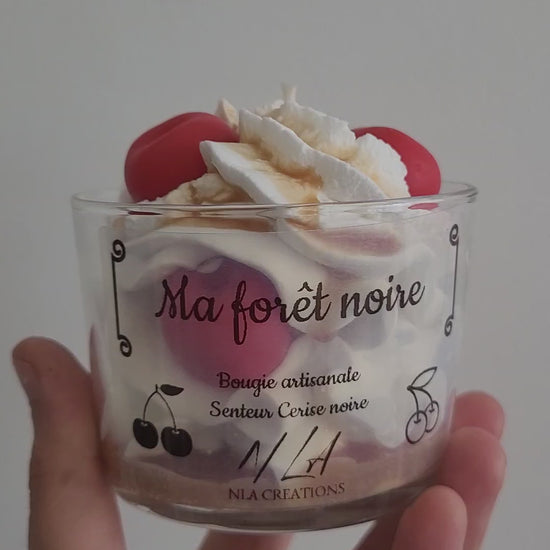 Vidéo gros plan montrant une bougie artisanale parfum Cerise Noire Intense, style forêt noire en pot, chantilly blanche avec cerise rouge brillante et coulis marron, révélant les détails gourmands et faits main.