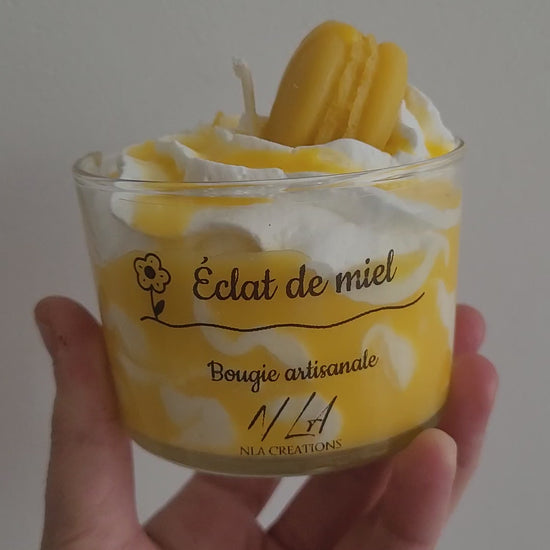 Vidéo d’une bougie artisanale couleur miel, décorée d’un macaron en cire sur une chantilly onctueuse. La caméra tourne autour du pot, mettant en valeur les détails et la texture crémeuse. Parfum doux et réconfortant de miel et avoine.
