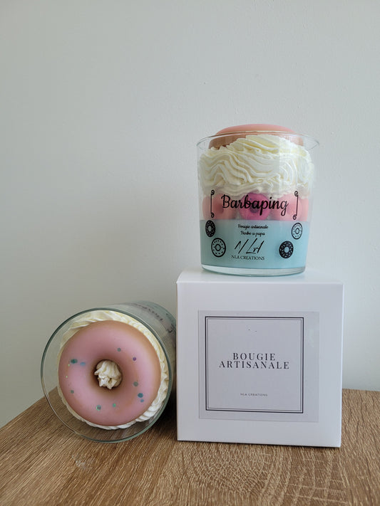 Bougie artisanale aux couleurs bleu pâle et jaune pâle, décorée de nombreux petits doigts rose fuchsia et surmontée d’un gros donuts rose vif, rappelant une gourmandise sucrée et joyeuse.