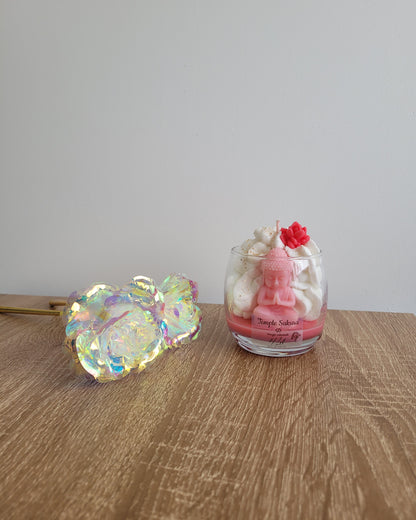 Bougie rose parfumée à la fleur de cerisier, coulée à la main dans un pot en verre avec une figurine de Bouddha et des paillettes dorées.