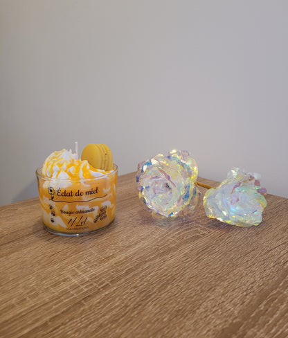 Bougie artisanale couleur miel, présentée dans son contenant en verre, avec un macaron décoratif posé sur la chantilly. Parfum Miel Avoine, ambiance douce et réconfortante.